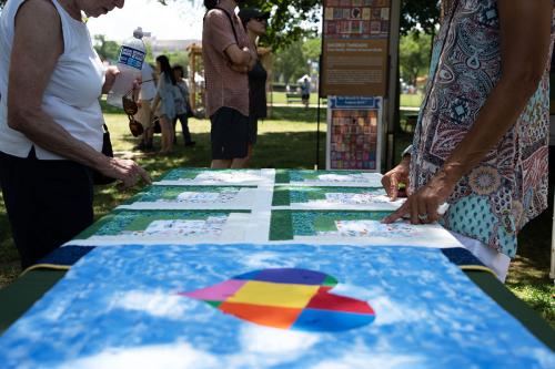 Two people, heads out of frame, stand on either side of a green and white quilt laid on a table outdoors.