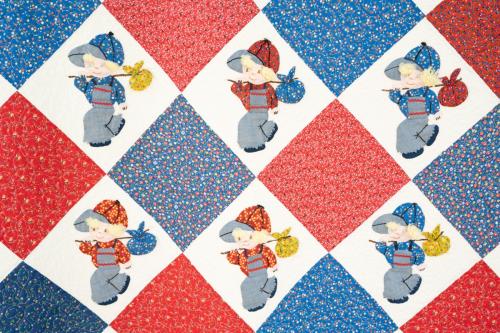 A close-up of a quilt with an alternating red, white, and blue speckled diamond pattern, with little children in red and blue caps and overalls holding bindles over their shoulders.