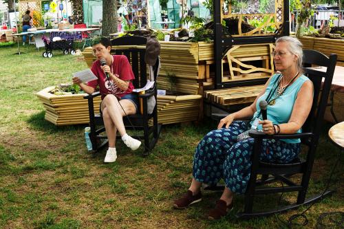Under a wooden structure with a sign that reads Teaching Garden, a woman speaks with a small group of people seated on benches.