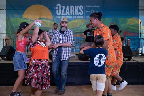 A group of six form a circle on a dance floor. A few of the dancers hold hands and spin as they move.