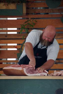 A man leans over a table as he cuts through a large piece of meat.