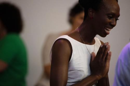 Among people dancing, a woman laughs and clasps her hands together as if clapping or in prayer.