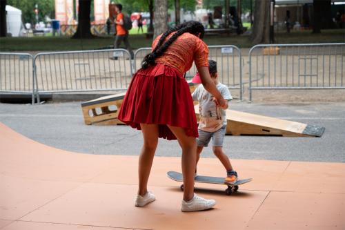 A woman in a red dress helping a young boy skateboard.