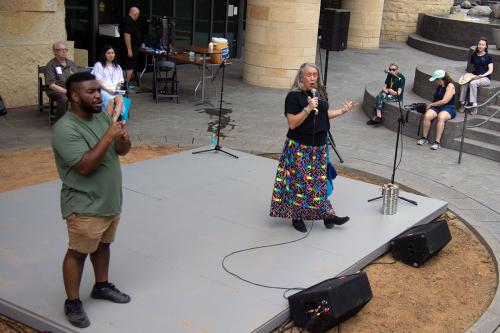 On an outdoor stage, a woman tells a story alongside an ASL interpreter.