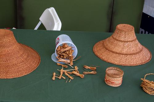 Display of items on a table, including two woven cone-shaped, flat-topped hats and several strips of bark knotted neatly together.