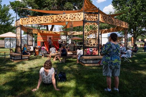 People sit in and around a shaded wooden structure among trees.