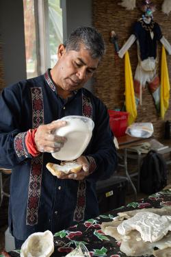 A man wearing a navy blue patterned shirt pours liquid plaster into a mold from a Tupperware container.