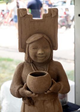 Close-up on an unfired, unglazed clay figure of a woman holding a pot.