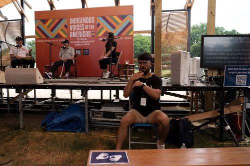 An ASL interpreter works sitting in front of a stage, where three people are engaged in conversation.