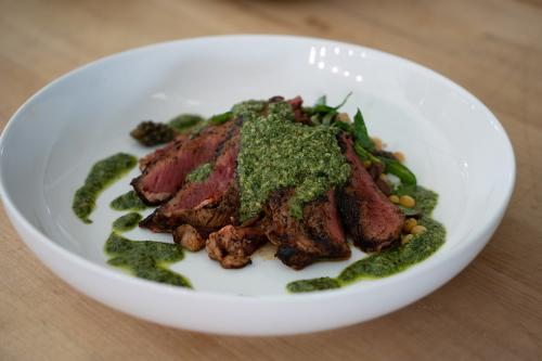 A bison flank steak sitting in a white bowl with a vibrant green sauce on top.