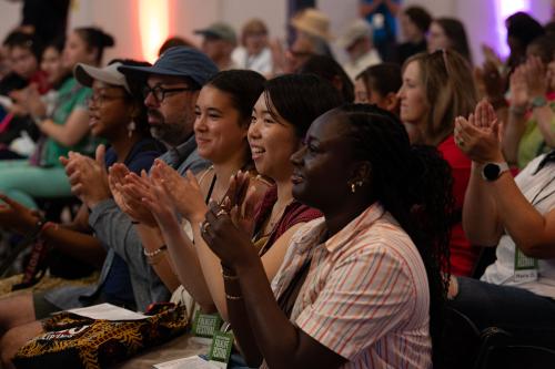 A crowd of people seated indoors smiles and claps.