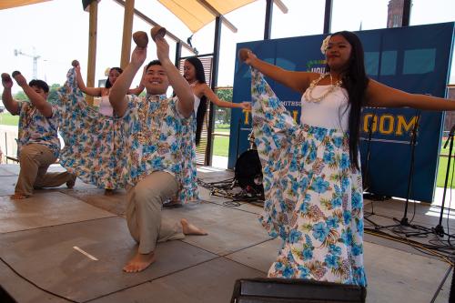 Five young students wearing blue and white regalia from the Northern Mariana Islands perform onstage; two of them kneel, while three fan their skirts.