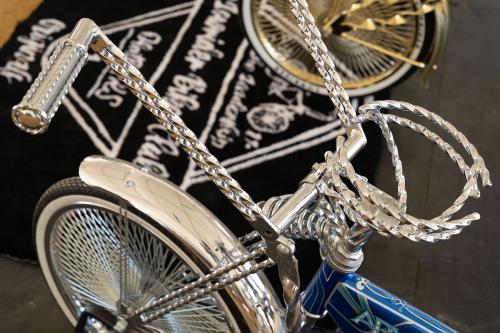 Close-up on the shiny chrome handlebars and front fender of a lowrider bicycle with a blue painted frame. 