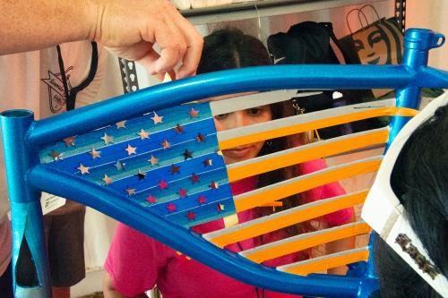 Through the stripes of the American flag in the bike frame, we set a young woman inspecting the bike.