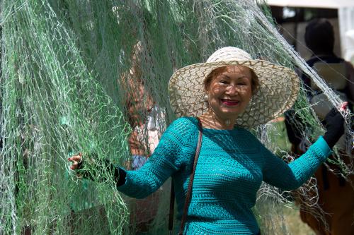 A woman in a hat is playfully caught in a light blue-green fishing net. Her arms are outstretched holding the net and she is smiling. 