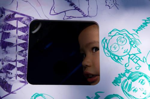Through a cutout in a white box, a small child peers out. Turquoise and purple drawings on the box.