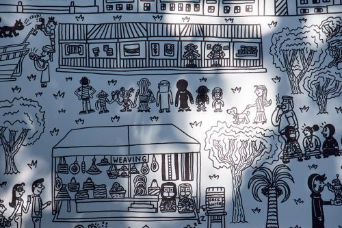 Black drawing on a white board, depicting festival tents, crowds of people, and trees. In the front, a tent marked WEAVING.