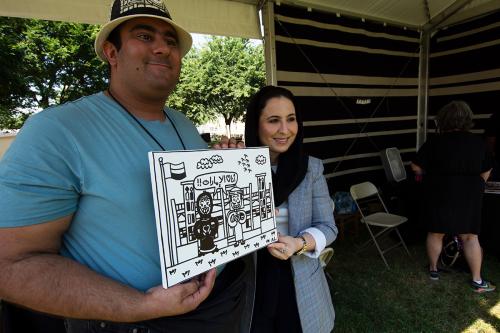 A man and a woman hold a black and white drawing of two individuals in front of a large building, while posing and smiling. 