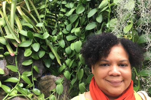 Profile of a woman outside, standing against a background of foliage.