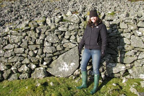 The young woman poses next to a stone wall and field of gray stones.