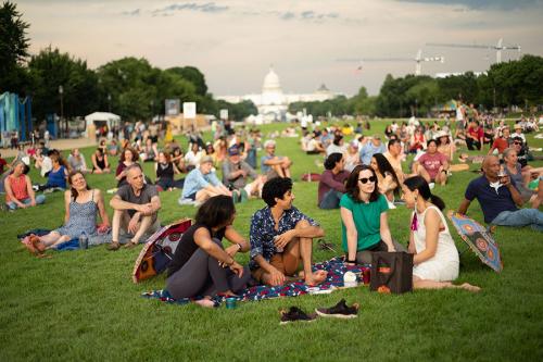A crowd sits on the green lawn of the National Mall, with the U.S. Capitol Building in the background.