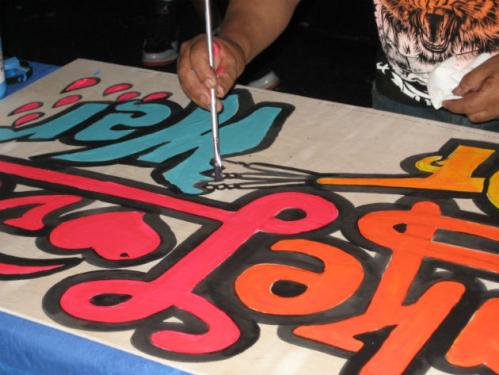 MONKY paints a "Make Love, Not War" sign at Chicha! A Peruvian Dance Party. Photo by Georgia Dassler, Ralph Rinzler Folklife Archives