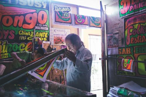 Chicha artist Monky shows his nephew how to sikscreen brightly-colored posters. Photo by Joshua Eli Cogan, Ralph Rinzler Folklife Archives