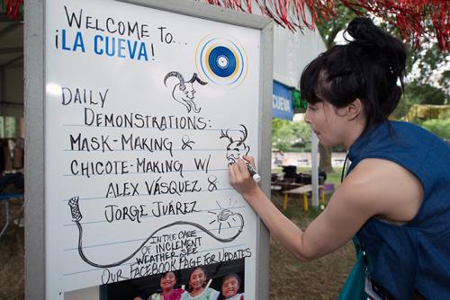 Each morning, Folklife Festival staff updates the daily schedules on whiteboard signs. Here's <em>Sounds of California</em> intern Katie Radishofski adding some <em>diablos</em> illustrations to La Cueva. Photo by Walter Larrimore,