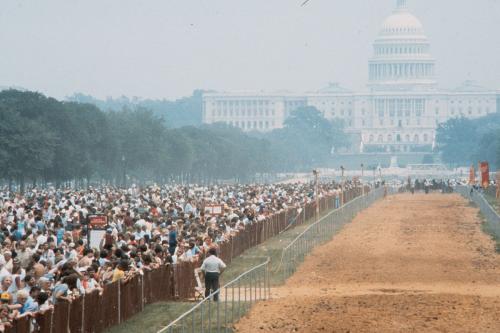 Outdoor horse race track with visitors lined up along the left side.