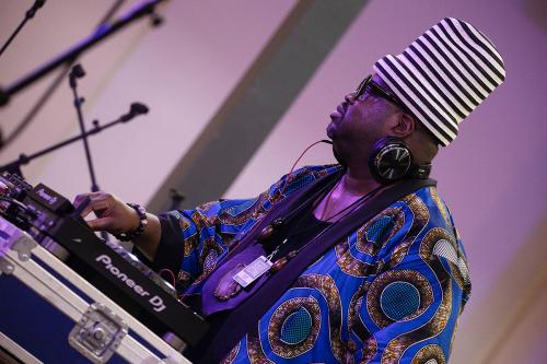 A DJ wearing a flowing blue top and tall, cylindrical white and black striped hat.