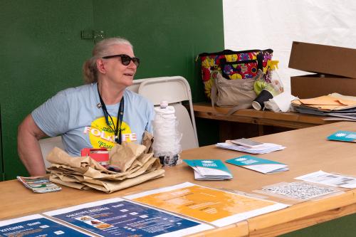 A woman smiles, sitting behind a counter with brochures, maps, and menus.