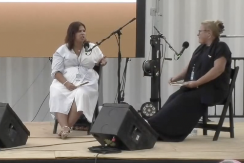 Two seated women speak into elevated microphones.