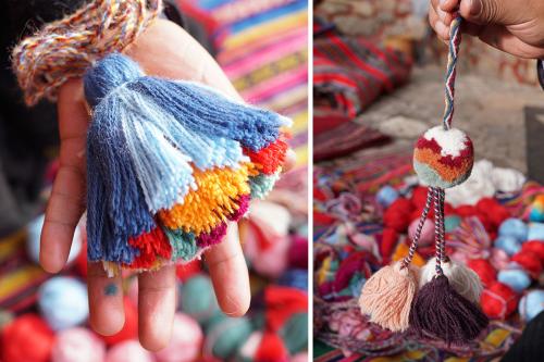 On the left, closeup of a hand holding up a multicolored yarn tassel. On the right, a hand holds up a yarn pom-pom.