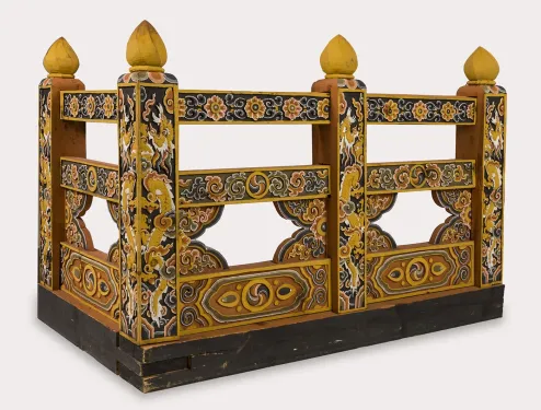 A corner section of a walkway railing with colorful, ornate designs covering the rail and posts—which are each topped with a tear-drop shaped finial.