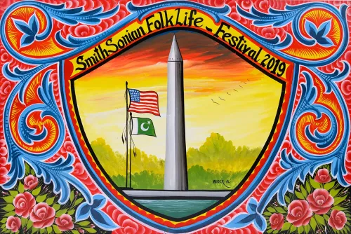 A colorful horizontal painting of the Washington Monument against a yellow and red sky, with two flags flying nearby. A shield-shaped frame surrounds the scene with the words “SmithSonian Folklife Festival 2019” and colorful floral and leaf designs filling the entire surface area.