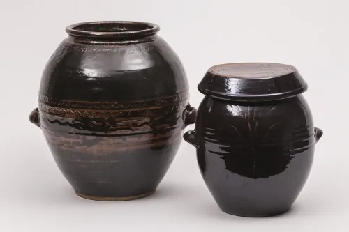 Two large, rounded earthenware jars with a shiny dark brown glaze and small, rounded handles on either side.
