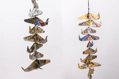 Two strings of eight, four-inch-wide origami whales folded from colorful patterned paper are pictured side by side in two separate photographs.