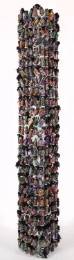 A rectangular plexiglass tower is covered by hundreds of small, colorful fabric dolls, each uniquely designed with fabric and beading.