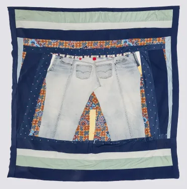 A patchwork quilt with navy blue border framing a pair of faded blue jeans at the center, surrounded by a variety of fabric scraps of different sizes and shapes in orange, blue, seafoam green, and white.