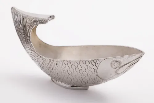 A silver vessel shaped like a fish with a curved tail as a handle and intricately carved details.