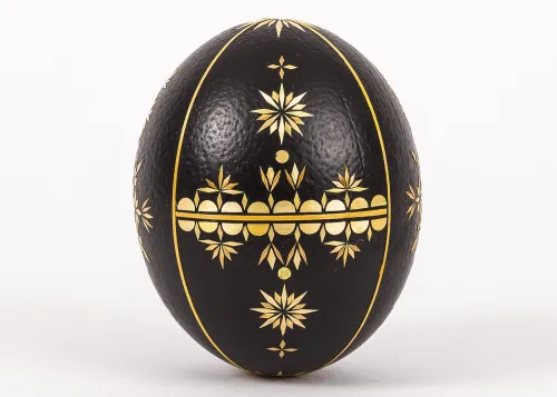 A dark brown ostrich egg standing on its narrow end, decorated with cut-straw designs.
