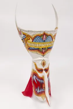 An elongated white mask painted with bright shades of red and orange, featuring a face with wide open mouth and sharp, bared teeth. “Long Live the King” is written in capital letters across the crown of the mask. 